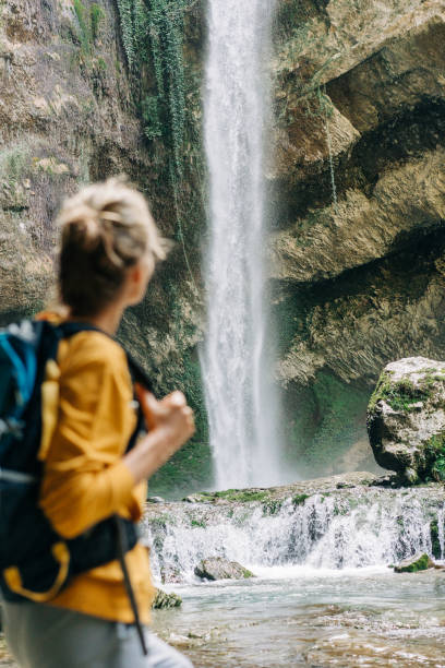 istock Defocused unrecognizable woman from behind with a backpack looking at a waterfall in a canyon. 1392799415