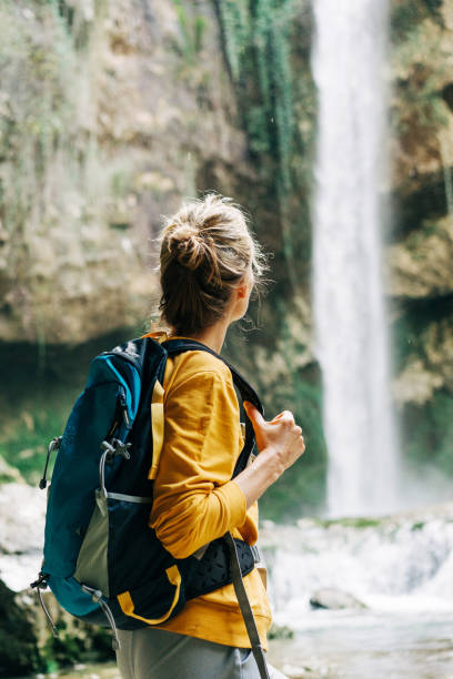 istock Young active unrecognizable woman from behind with a backpack looking at a waterfall in a canyon. 1392799451