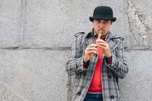 A man musician plays a wooden instrument on the street against a gray wall. Urban lifestyle.