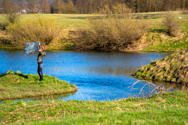 widok z boku kobiety stojącej i bawiącej się szalikiem, ciesząc się wiosennym słońcem i wodą jeziora planinsko polje, słowenia - planinsko polje zdjęcia i obrazy z banku zdjęć