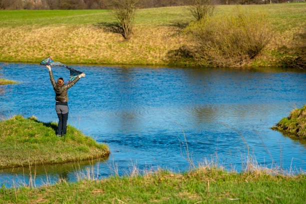 vista para trás da mulher em pé e se divertindo com um cachecol enquanto desfrutava do sol da primavera e da água do lago planinsko polje, eslovênia - planinsko polje - fotografias e filmes do acervo