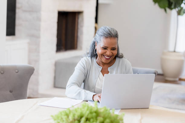 istock Smiling woman sits at dining room table to use laptop 1392802414