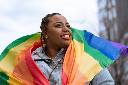 Confident black woman outdoors holding a rainbow flag