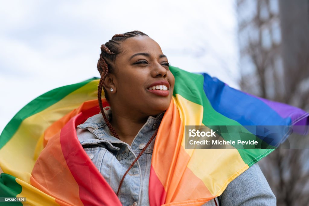 Confident black woman outdoors holding a rainbow flag LGBTQIA Rights Stock Photo