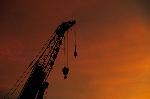 Close-up silhouette industry giant crane working on construction building site from downtown on twilight sky nature background, copy space
