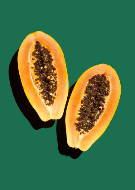 Ripe papaya in the cut, two halves on a green background, hard light, isolated