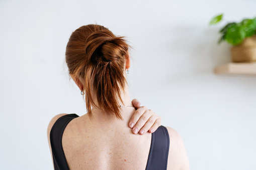 a red-haired woman kneads her shoulder. view from the back