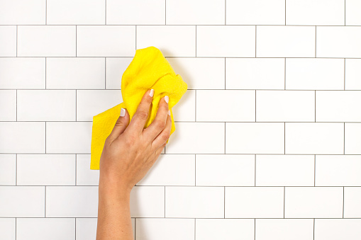 Woman hand cleaning a white subway tiles kitchen wall with a sponge cloth