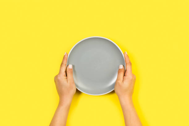 istock Woman holding with both hands a gray ceramic round plate on a yellow background 1392808111