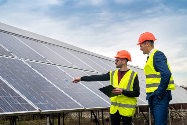 two young workers in overalls and helmets check the installed solar panels. stock photo