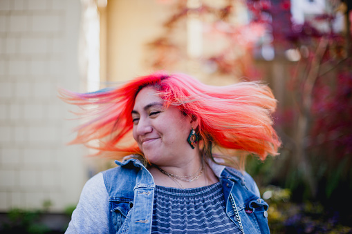 Portrait of a young woman with vibrant colored hair spinning around and tossing her hair. Shot with a 50mm lens, using all natural light, taken outdoors.