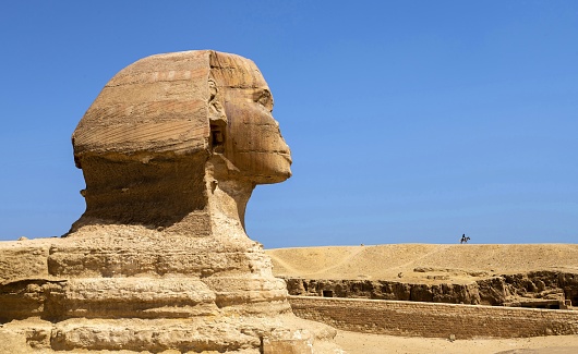 Giza, Egypt, April 15, 2022: View of the Great Sphinx of Giza on a sunny spring day. It is a limestone statue of a reclining sphinx, a mythical creature with the head of a human, and the body of a lion. The pyramid field of Giza is listed as UNESCO World Heritage Site.
