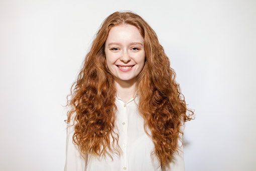 Close-up studio portrait of an attractive 20 year old red-haired woman in a white shirt on a white background