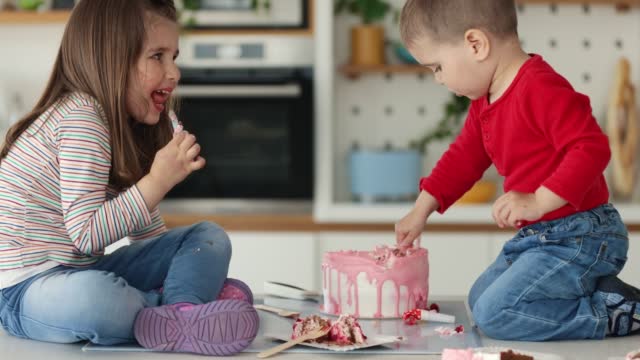 Brother and sister playing with cake while nobody's watching.