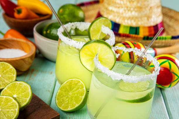 Happy Cinco de Mayo with two Lime Margarita Glasses on a Colorful Slated Wood Background This is a photograph of two modern lime margarita glass with a rim of salt surrounded by fresh cut limes and chilis on a colorful Slated Wood Background next to a sombrero margarita stock pictures, royalty-free photos & images