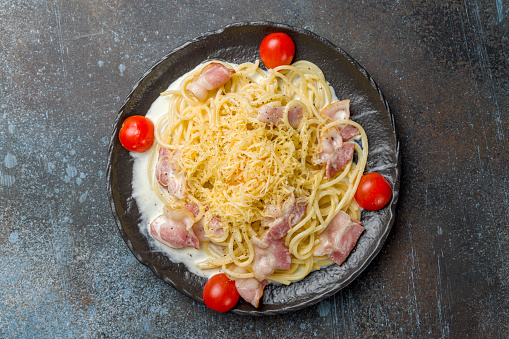 Spaghetti Carbonara with bacon on black plate on dark blue stone table top view