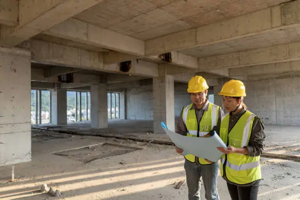 Photo of Male and female construction engineers with drawings comparing data