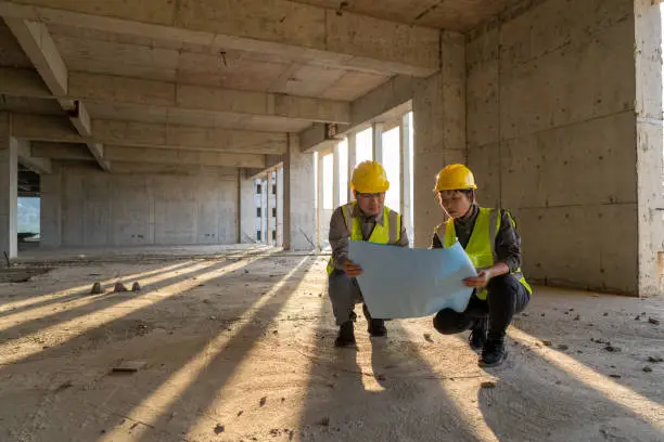 Photo of Male and female construction engineers with drawings comparing data