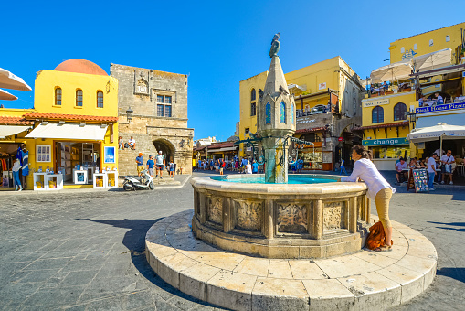 A female tourist washes her hands in the Castellania fountain in Hippocrates or Ippokratous Square in the historic center of Rhodes on the island of Rhodes, Greece.