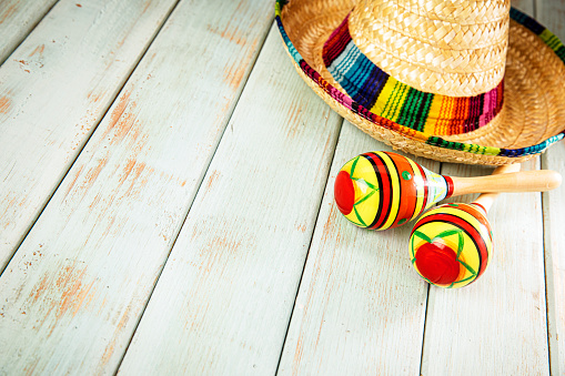 This is a photograph of a sombrero and two maracas on a colorful Slated Wood Background next to a sombrero