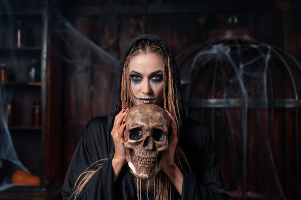 istock Halloween concept. Witch portrait close up with dreadlocks looking camera dressed black hood standing dark room with cage on background 1392846628