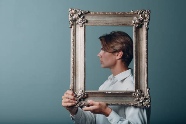 istock Portrait young man standing with picture frame at studio. 1392848588