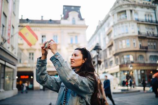 Young tourist woman on a city break, using her smartphone to snap some photographs.