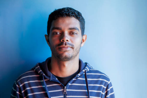 Young man looking at camera and smiling. Brazilian boy looking at camera on blue background. People concept. Man concept.