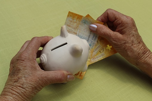 hands of an older woman holding Swiss banknotes and piggy bank