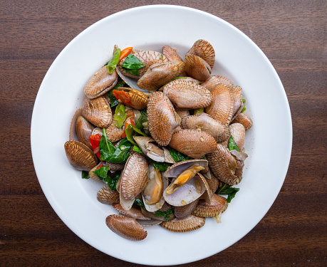Stir-fried clams are seafood. Fried with basil and chili to taste delicious. On a white plate Lay on the wooden floor Ready to eat It is a popular dish with Thai and Asian people.