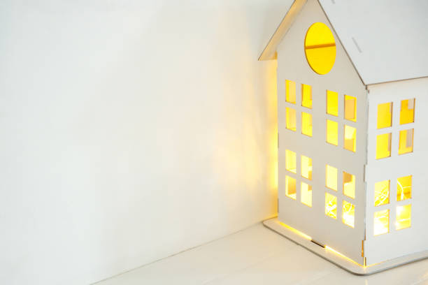 white wooden house with yellow light from the windows, on a white background. Home comfort concept. Mortgage and rental of apartments