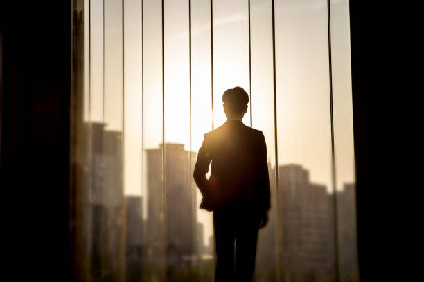 istock businessman looking out from a large window in the office 1392869258