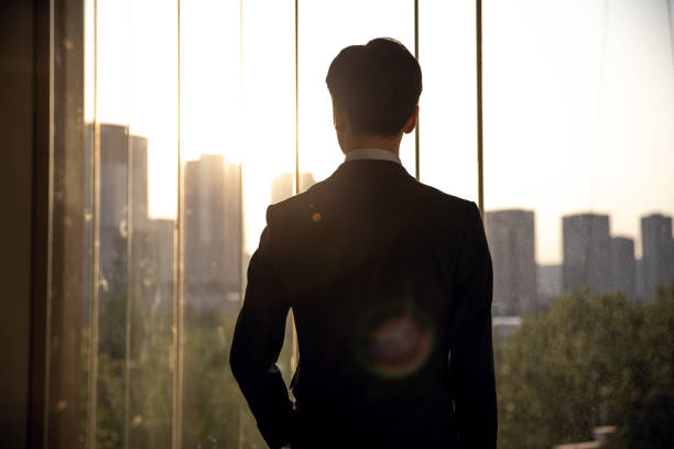 istock businessman looking out from a large window in the office 1392869277