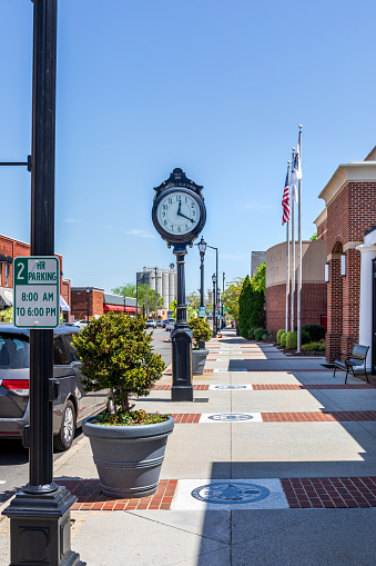 Mooresville, NC, USA-17 April 2022: Vertical view down sidewalk past Charles Mack Citizen Center, showing large clock, with Bay State Milling in the distance.