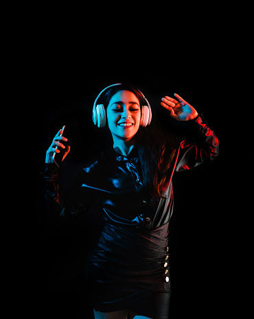 latin young woman with headphones listening to music over color neon and black background in Mexico Latin America