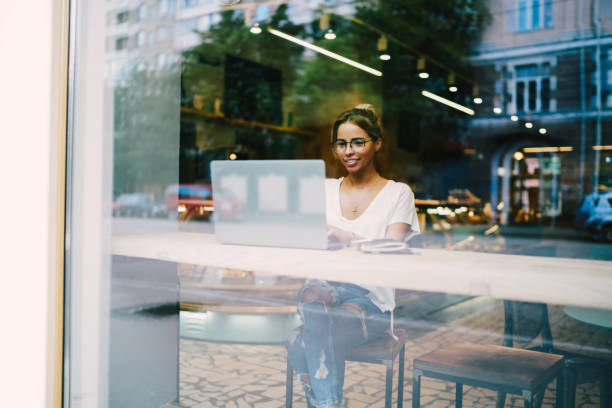 istock Positive graphic designer in optical eyeglasses watching webinar for improving skills on internet website sitting in coffee shop and using free wifi connection.Cheerful copywriter working freelance 1392882376