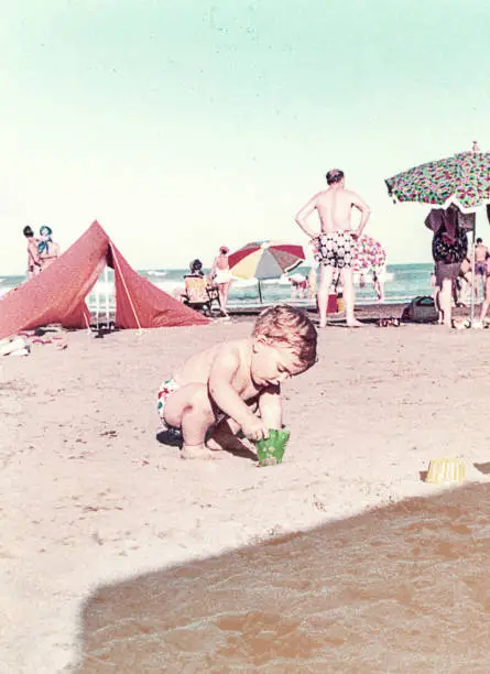 Vintage baby at the beach playing with the sand. Vintage image from the seventies. Summer family resort.