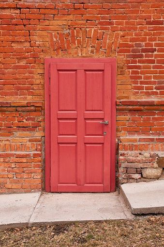 A red door in a cracked brick wall, next to a concrete walkway
