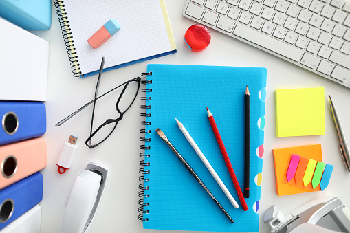 Top-view of worker preparing to working day. Glasses, datebook,computer keyboard, folders and colorful bookmarks on table. Pencils lying on diary. Business and company concept
