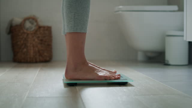 Legs of unrecognizable woman stepping on the bathroom scale. Shot with RED helium camera in 8K.