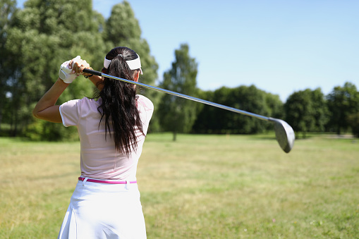 Close-up of golf player with driver teeing-off in tournament competition. Golf course for winner. Comfy outfit and perfect grass field. Sport game and woman champion concept