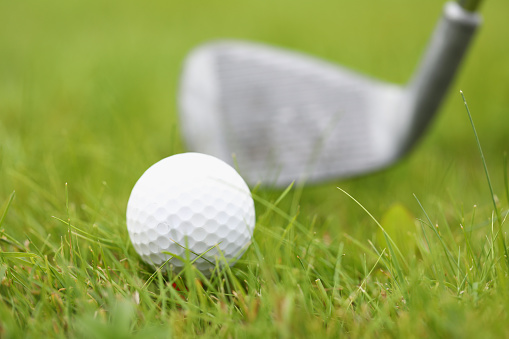 Close-up of white golf ball and club laying on green grass. Macro shot of equipment for game. Competition and tournament. Fresh field for play. Luxury sport concept