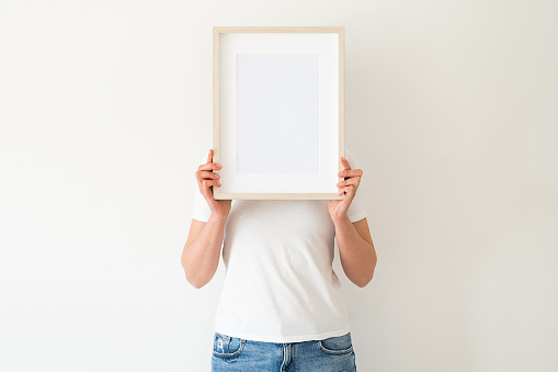 A wooden frame with empty space in women's hands. Mockup for your design. Clean white space for your presentation. Layout for ads. Template for demonstration and presentation.