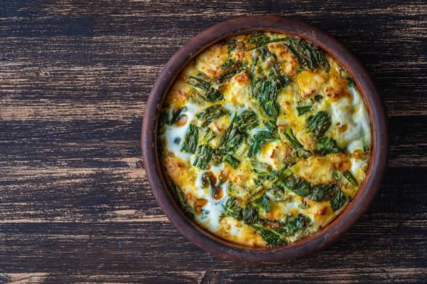 Ceramic bowl with vegetable frittata, simple vegetarian food. Frittata with egg, pepper, onion, cheese and green wild garlic leaves on table stock photo