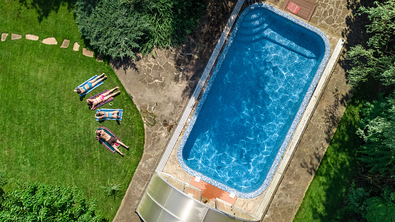 Happy family relaxing by swimming pool in summer garden, aerial drone view from above of parents and kids have fun on vacation, family weekend on resort