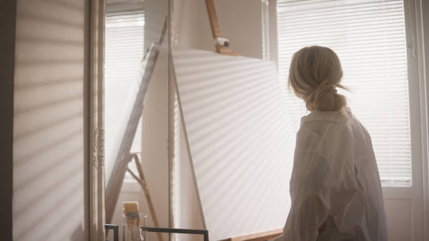 A woman and her home studio, where she paints and creates her work of art. A small little studio space by the window in her little apartment.