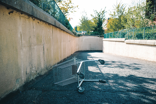 An abandoned shopping cart tipped over on its side, in the middle of an urban road in the city. Room for copy space.
