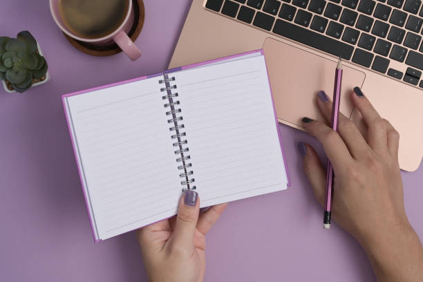 istock Woman hand holding notebook and using laptop computer on purple background. 1392897723