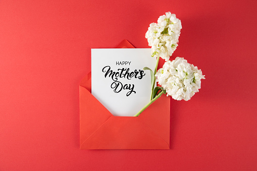 White flowers in red envelope with mothers day greeting card on red background
