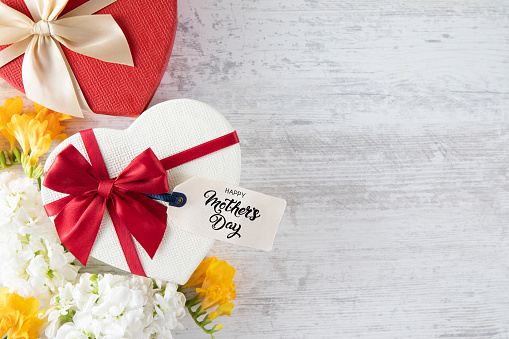 Happy Mother's Day gift tag with white florals and gifts on white wooden background.
